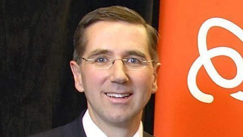 A man with brown hair and glasses looks straight ahead at the camera.