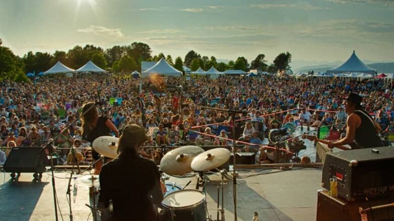 Hundreds of people at a festival watch a band perform. 