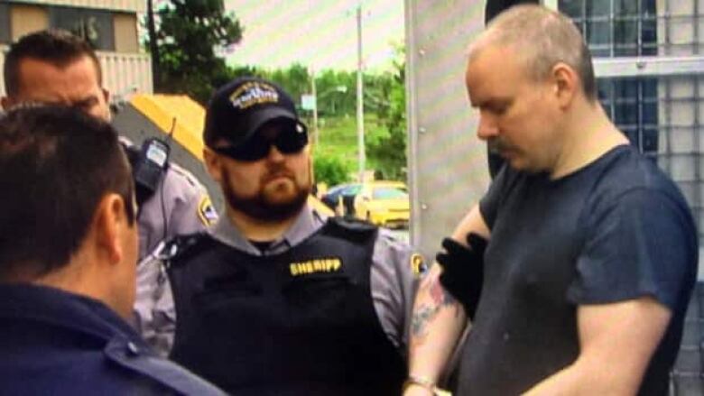 A man in handcuffs is shown with a sherrif's deputy.