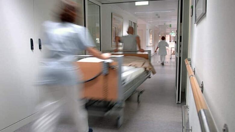 Nurses wearing scrubs wheel a bed down a hallway.