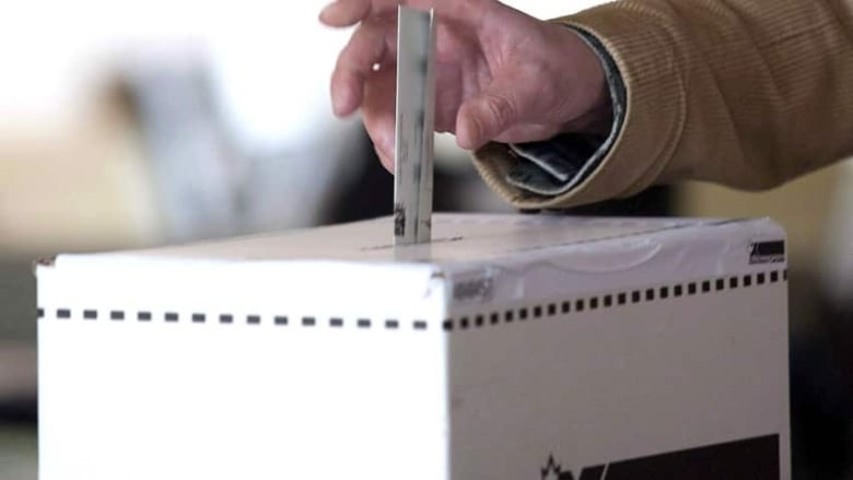 A hand drops an election ballot into a box.