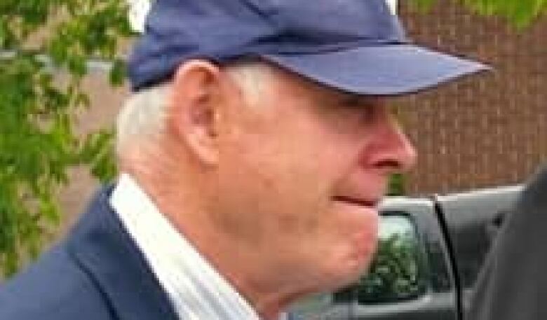 A side view of a man with white hair wearing a dark blue baseball cap.