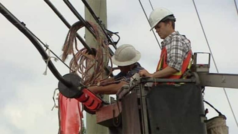 Men in hard hats atop a cherry picker fixing wires on a large pole.