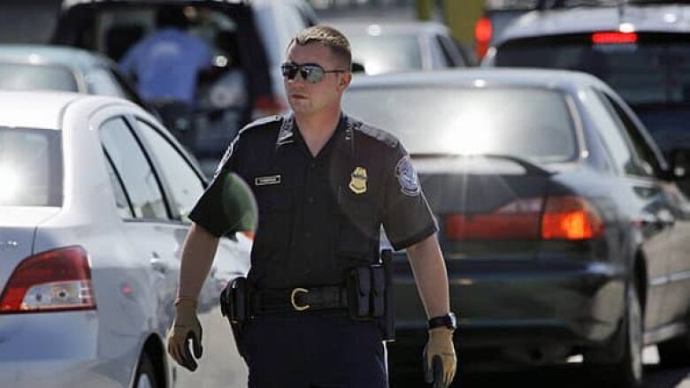 A U.S. Customs and Border Protection officer walks through a line of cars