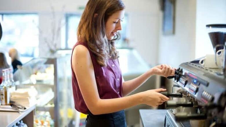 Young, female barista turns dials on a machine.