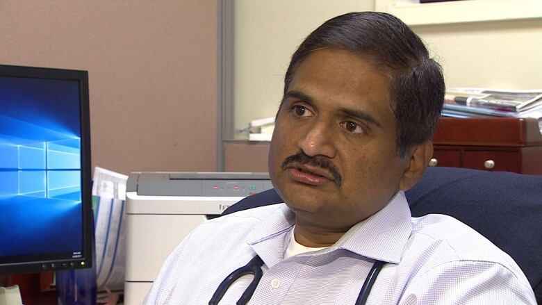 Headshot of a doctor with a stethoscope around his neck and a computer screen behind him. 