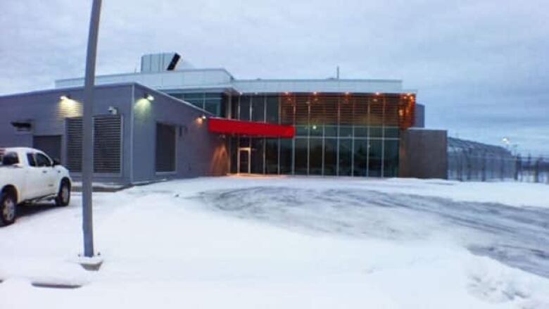 A grey building with large floor-to-ceiling windows. Snow is on the ground outside.