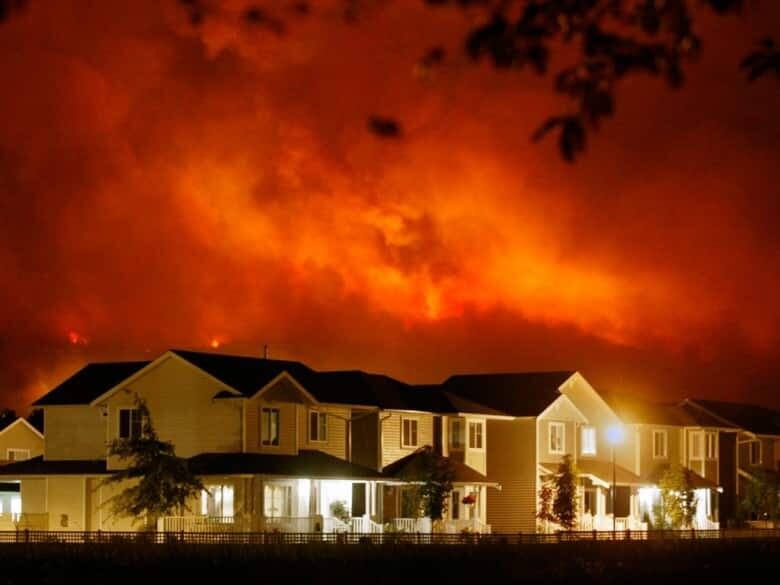 Flames rise behind houses under a dark sky.