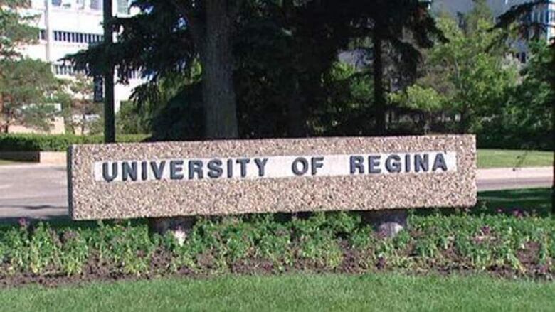 stone sign with University of Regina written on it. Grass in foreground. Spruce tree behind the sign.