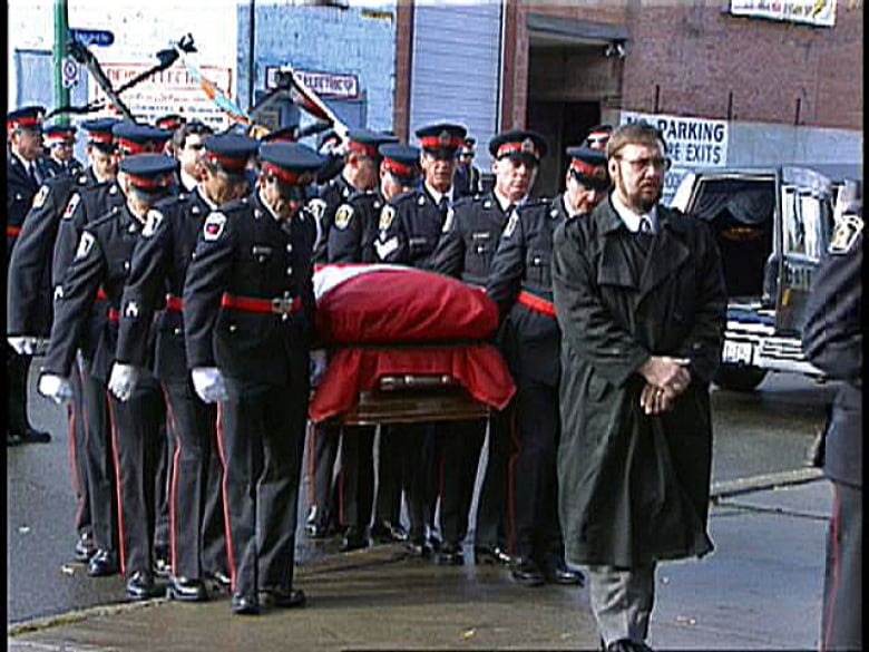 Police officers carry a casket draped in a Canadian flag.