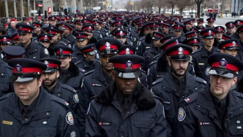 A crowd of over a hundred uniformed Toronto police officers are assembled at a ceremony on a city street