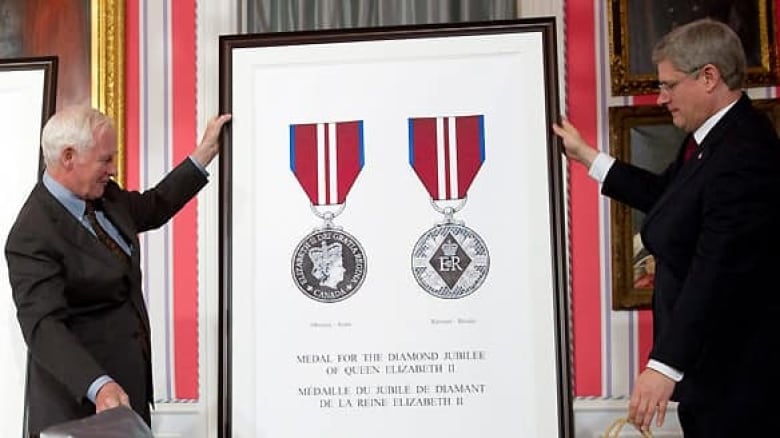 Two people hold a large photo depicting a medal.