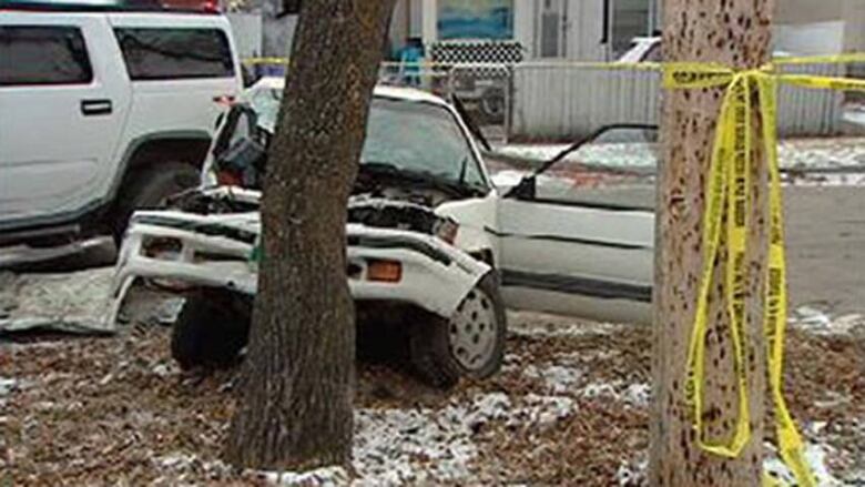 A white subaru is seen smashed into a tree with yellow police tape around it.