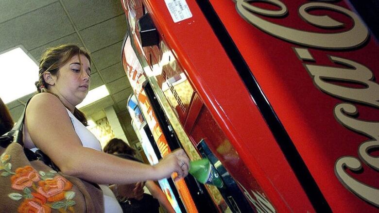 A woman withdraws a Coke from a vending machine. 