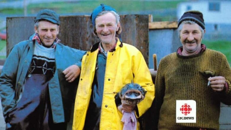 Three men dressed in fishing gear smile.