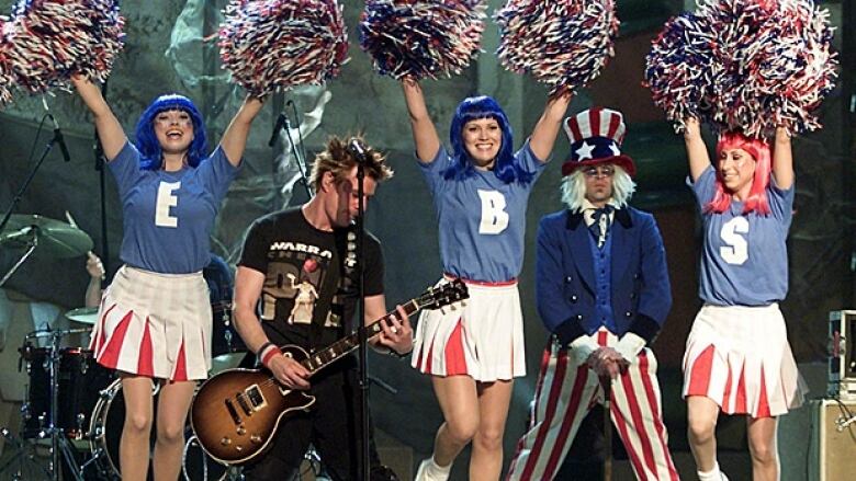 Cheerleaders and Uncle Sam on stage with a man playing guitar