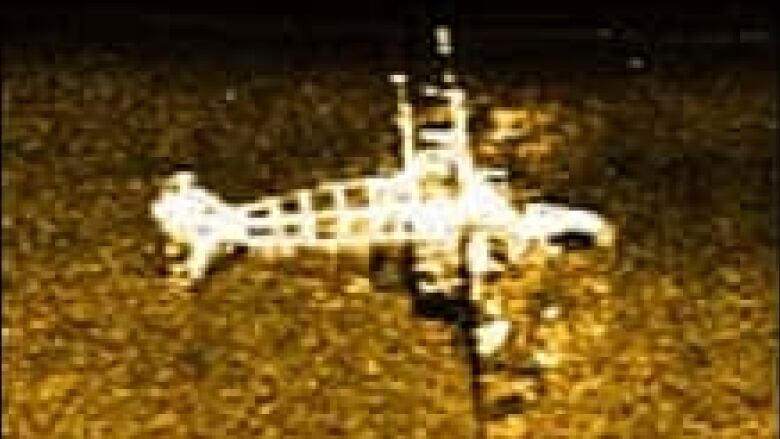 A pixelated brown-and-white image shows a disintegrating plane that appears to be partly buried.