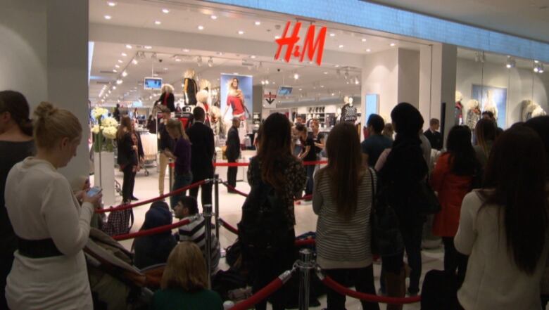 People standing in long lineup to enter a store. 