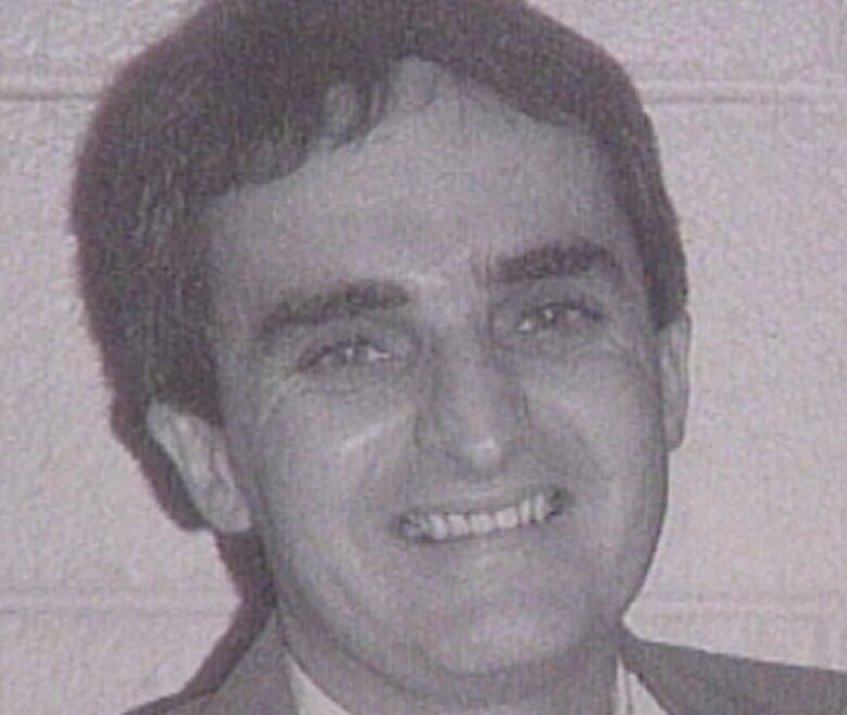 A smiling man with dark hair looks into the camera in a black and white photo