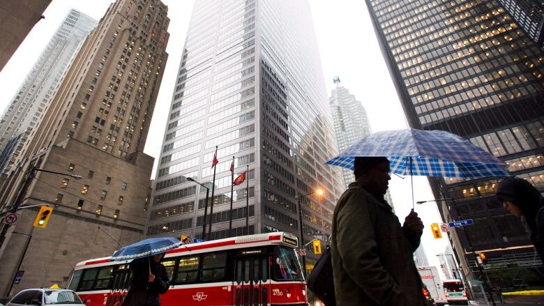 People carrying umbrellas walk past office towers.