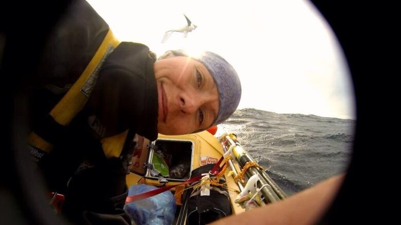 A woman in a small boat leaning over and smiling into the camera. She's out on the ocean.