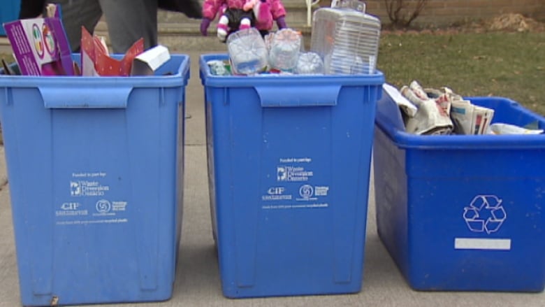 Three blue recycling bins sitting on a curb. 