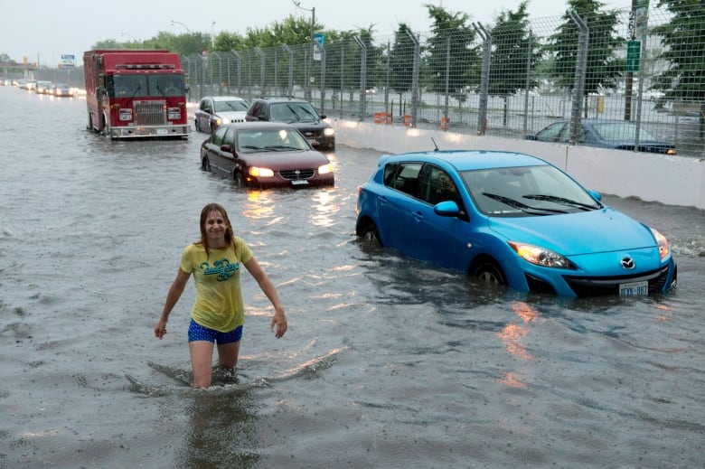 A woman wades through flood water on Lakeshore West during a storm in Toronto on Monday, July 8, 2013.