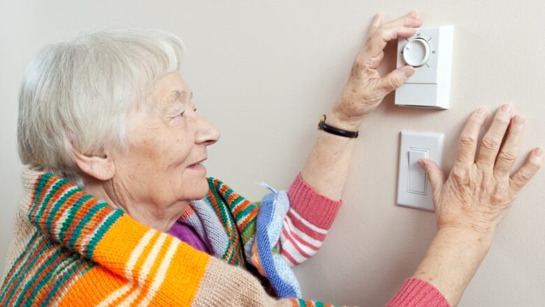 Senior woman adjusting her thermostat.