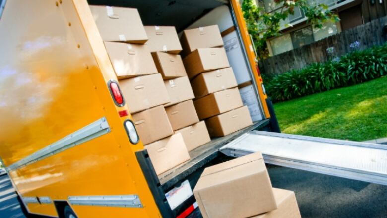 A yellow moving truck, opened at the back, shows stacks of cardboard boxes.