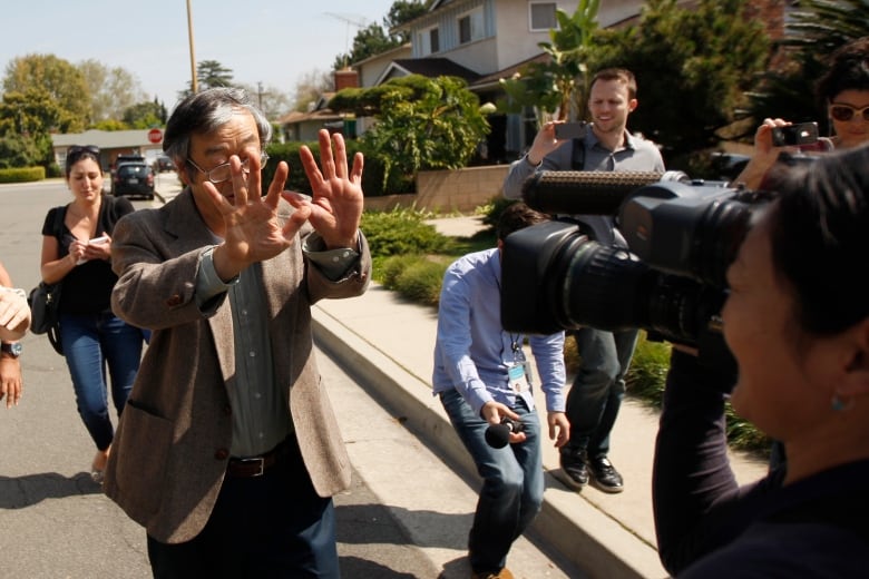 A man holds his hands up to block cameras.