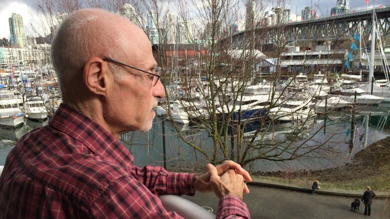 A man looks from his balcony, across a harbour filled with boats.