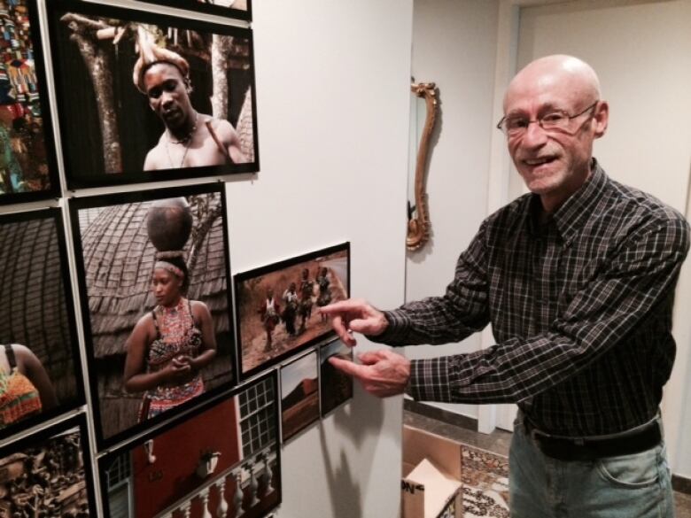 A man points to framed photographs on a wall in his home.