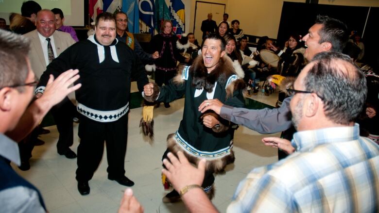 Men, some in traditional clothing, with gleeful expressions in a room. 