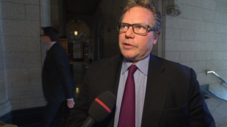 A man answers questions from reporters in the halls of the House of Commons.