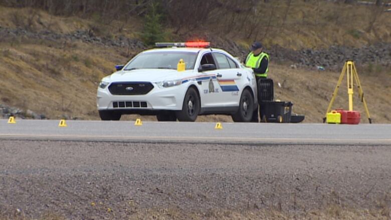 An RCMP officer and his vehicle are on a highway with evidence markers on the road.