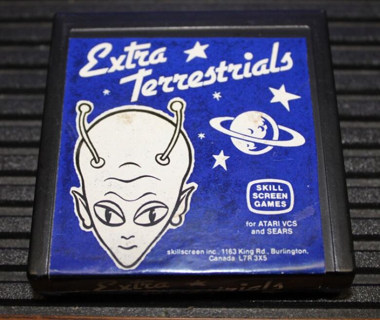 Close up shot of a vintage video game cartridge with art of an alien's head on top of a blue background.