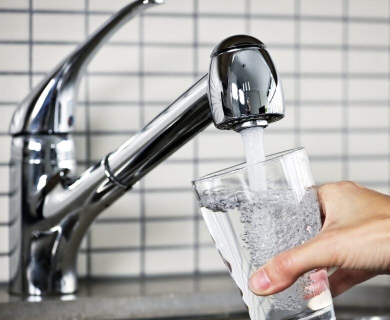 Person filling glass of water at tap.