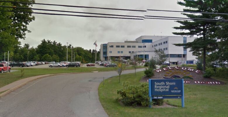 A blue sign reads South Shore Regional Hospital by the driveway leading to a large white and blue hospital, with cars in a parking lot