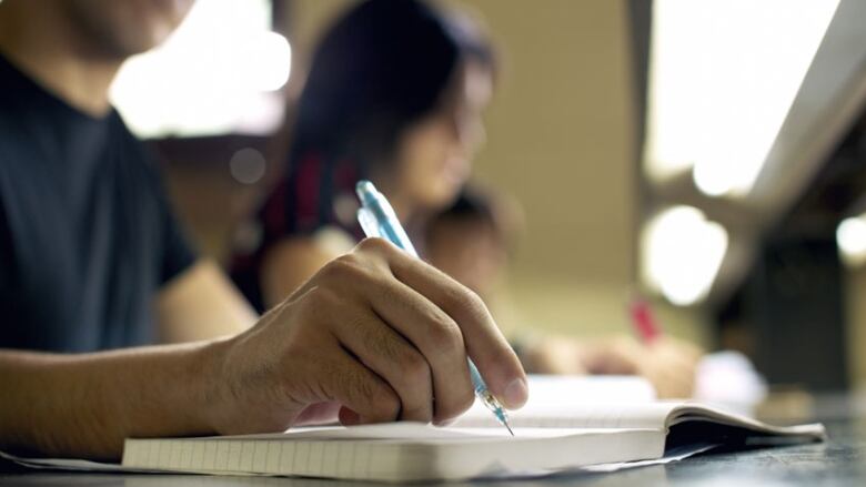 A closeup of a hand holding a mechanical pencil over a notebook. 