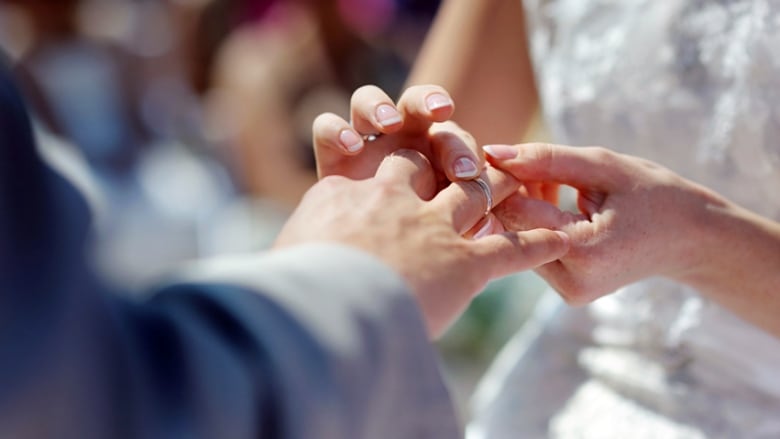 A closeup shows a bride's hands placing a wedding band on her new husband's finger.