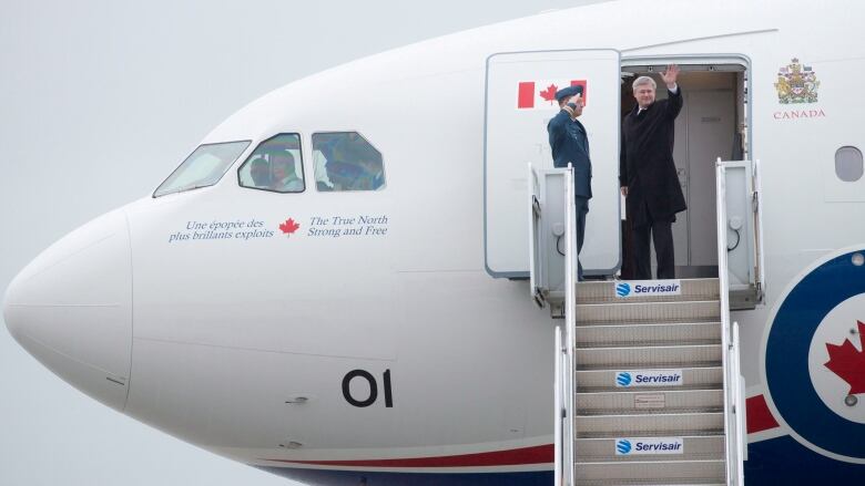 A man waves from the steps as he prepares to board a plane.