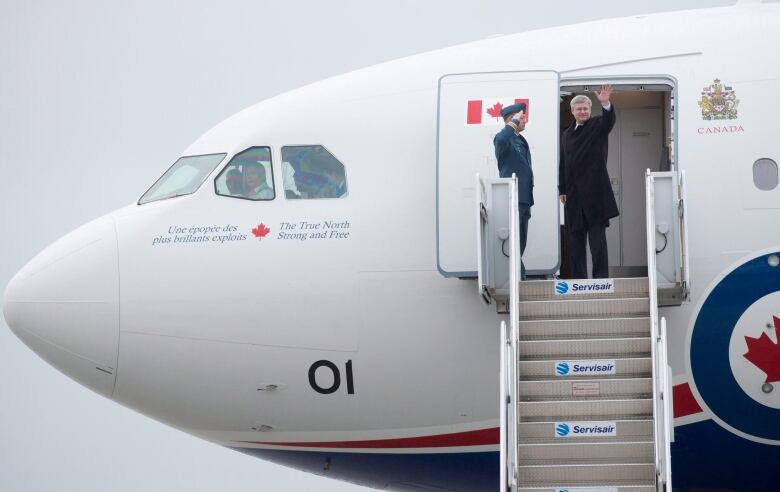 A man waves from the steps as he prepares to board a plane.