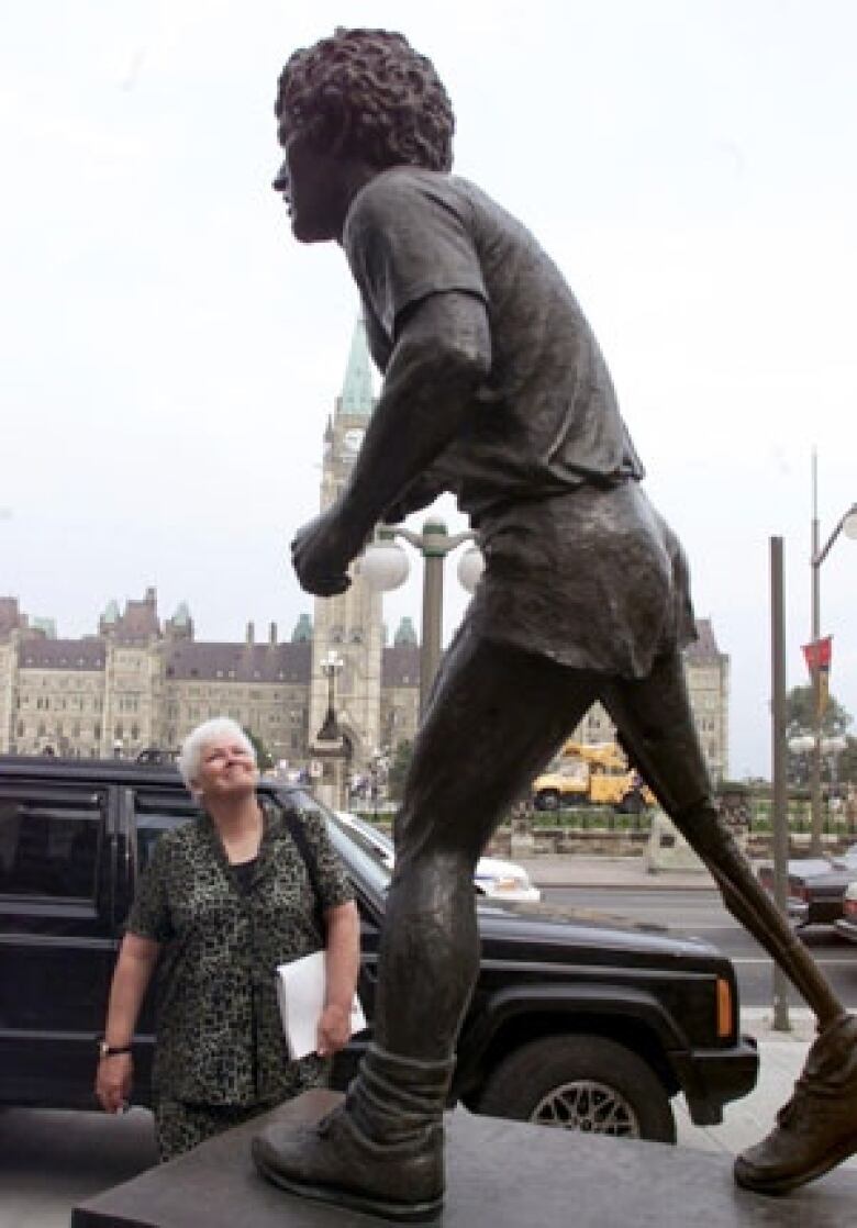 A woman looks at a statue of a runner near a legislature.