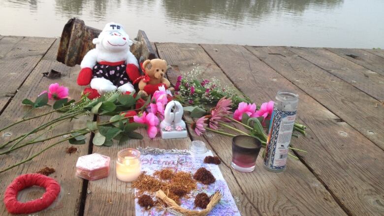 Flowers, tobacco, candles and teddy bears sit on a dock.