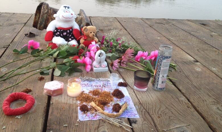 Flowers, tobacco, candles and teddy bears sit on a dock.