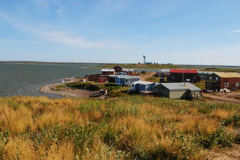 A photo of Tuktoyaktuk, Northwest Territories with tundra in the foreground and houses in the background with the ocean to the left 