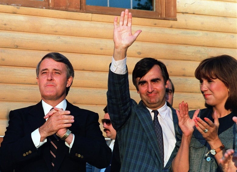 Two men in suits wave to a crowd.