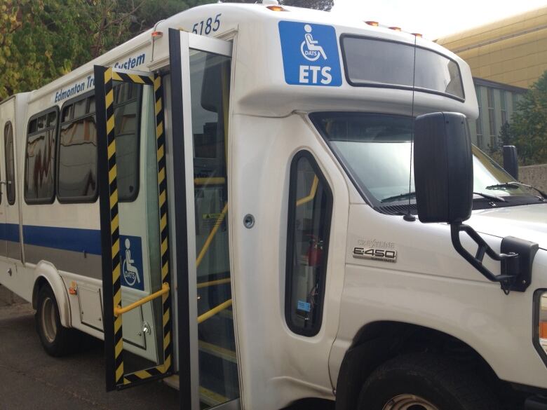 A white and blue bus is parked on a street with door open. 