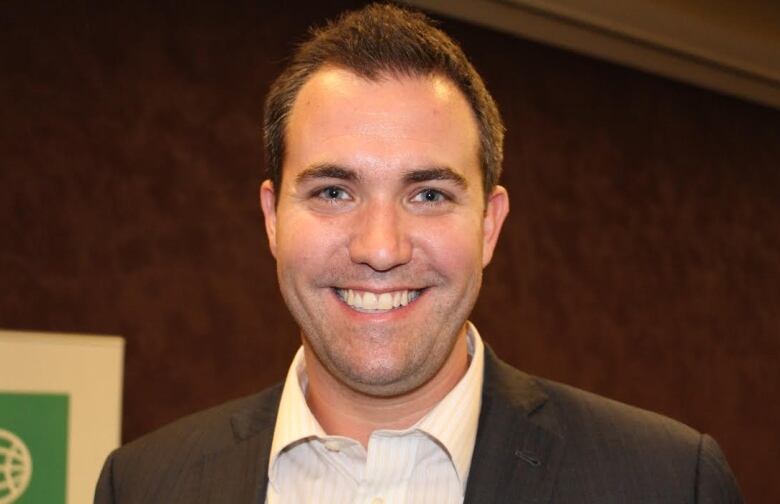 A man wearing a brown suit jacket smiles at the camera.