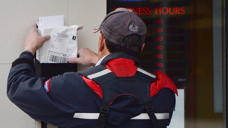 A Canada Post employee puts mail in a mailbox.